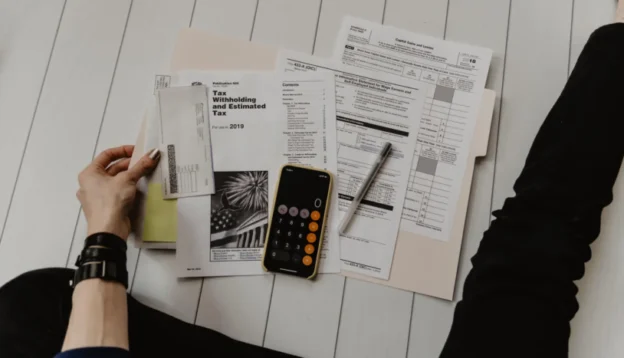 Osoba z dokumentami i kalkulatorem, próbuje obliczyć, jakie są koszty założenia firmy i prowadzenia działalności gospodarczej