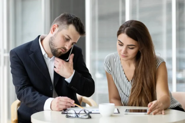 Kobieta siedząca przy biurku i mężczyzna rozmawiający przez telefon - Jak założyć własną firmę