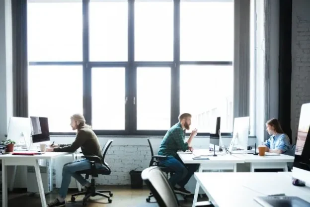 Pracownicy siedzący przy przed komputerami w biurze - Optymalizacja kosztów w firmie - dlaczego warto skorzystać z biura serwisowanego